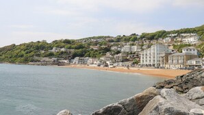 Un pueblo costero con edificios en una ladera, una playa de arena y un litoral rocoso.
