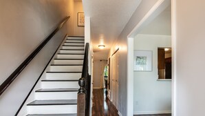 A staircase with a wooden handrail, leading to a room with a wooden floor and a door with a white frame. - The Fern & Fable - King Bed/TownHome with Deck (Birmingham)