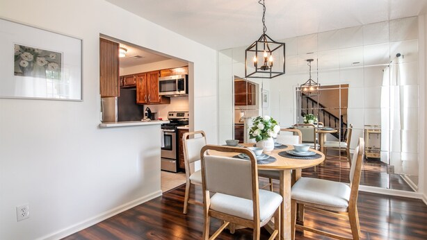 A modern kitchen with wooden cabinets, stainless steel appliances, and a dining area with a round table and chairs. - The Fern & Fable - King Bed/TownHome with Deck (Birmingham)