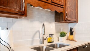 A kitchen with white subway tiles, stainless steel sink, wooden cabinets, and a countertop with a dish soap dispenser and a knife holder. - The Fern & Fable - King Bed/TownHome with Deck (Birmingham)