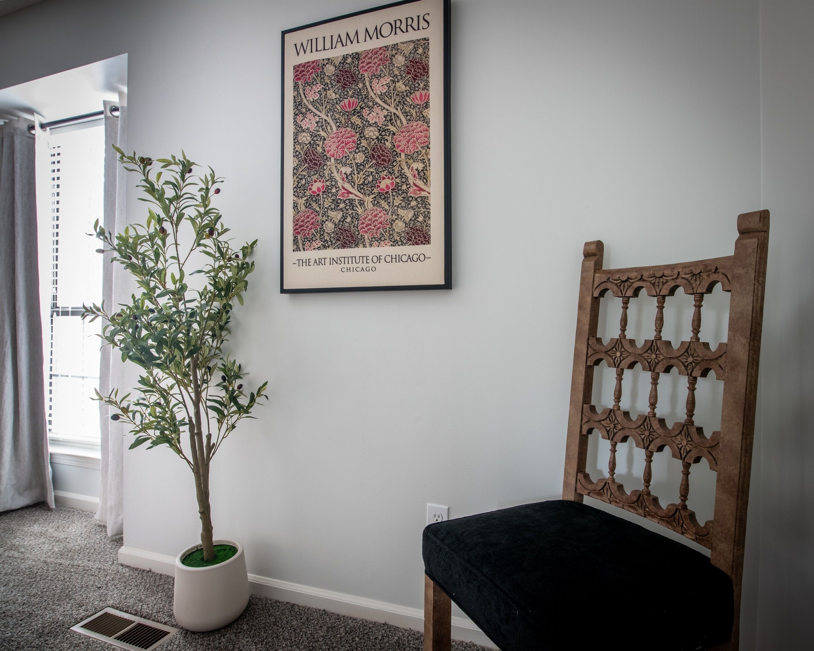 A room with a potted plant, a framed artwork, and a wooden chair.
