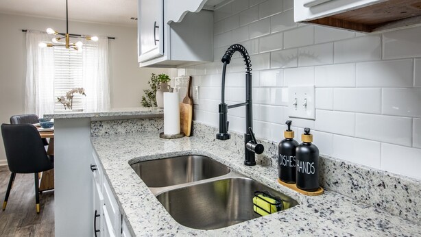 A kitchen with white cabinetry, a granite countertop, stainless steel sink, and black soap dispensers.