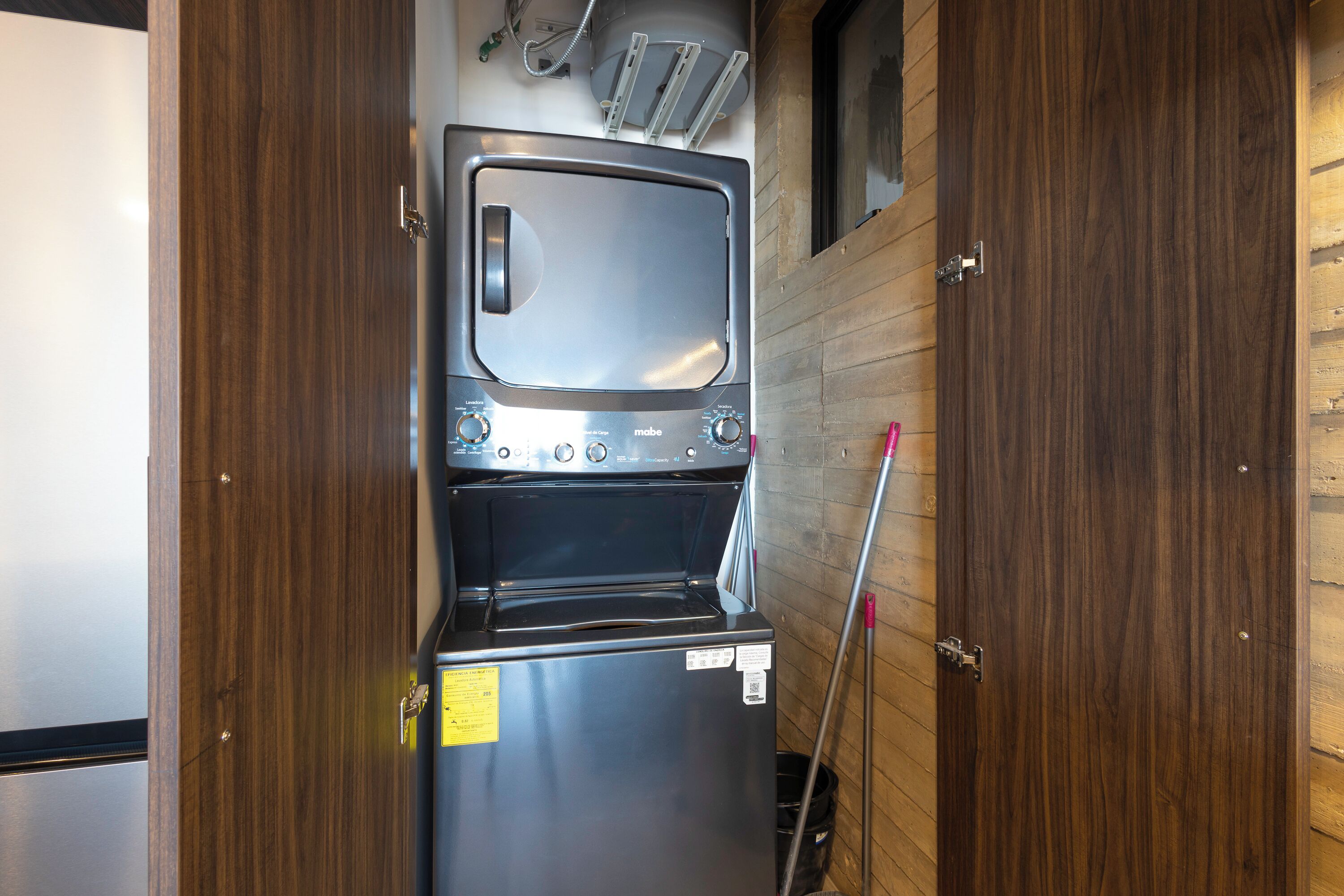 A compact kitchenette with a built-in oven and microwave, wooden walls, and a metal door.