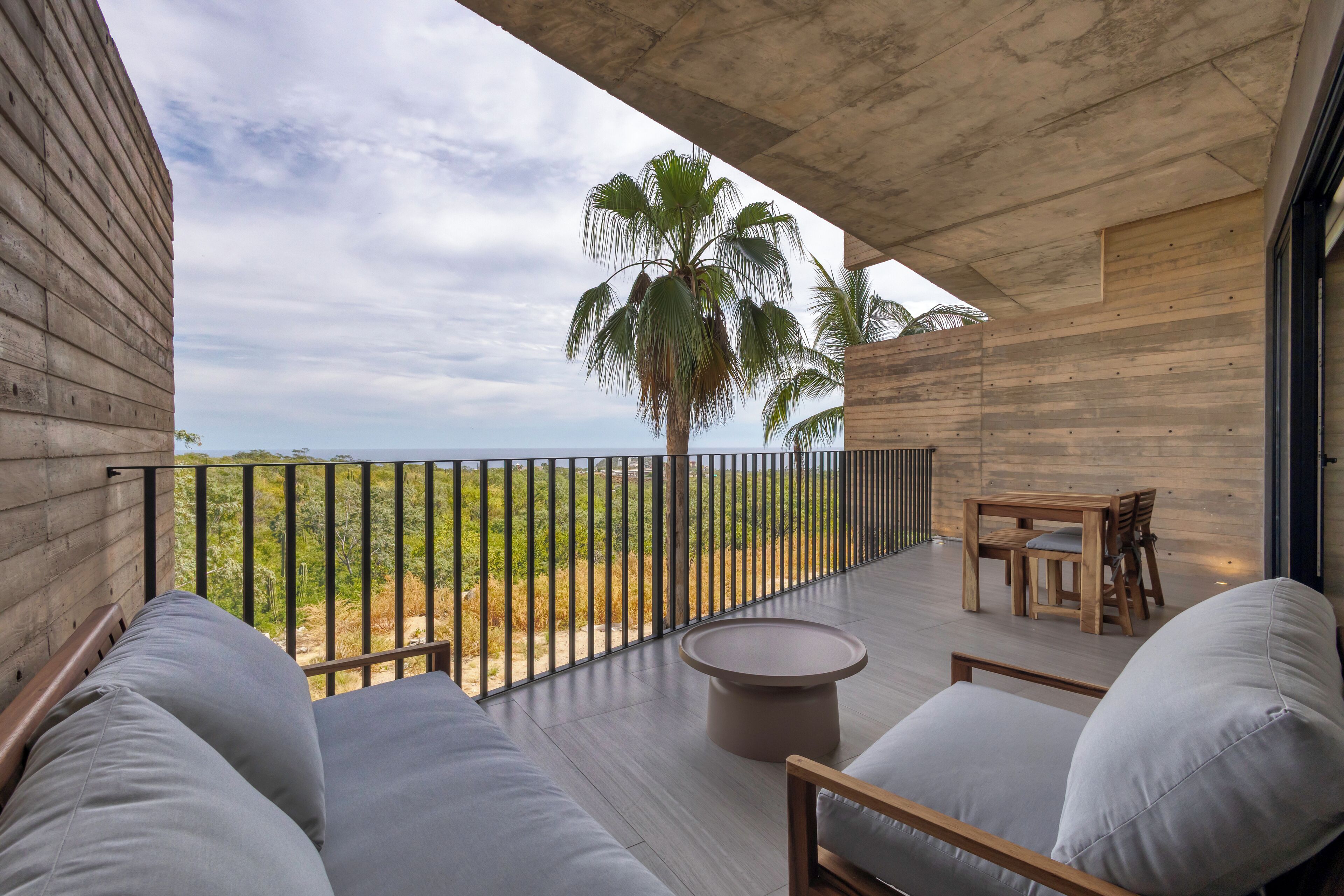 Ein Balkon mit Blick auf den Ozean, Holzmöbel und eine Palme.