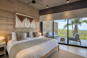 A modern bedroom with a large bed, a ceiling fan, and a balcony with a view of palm trees. - OR Cabo Boutique Residences by Lumina (Cabo San Lucas)