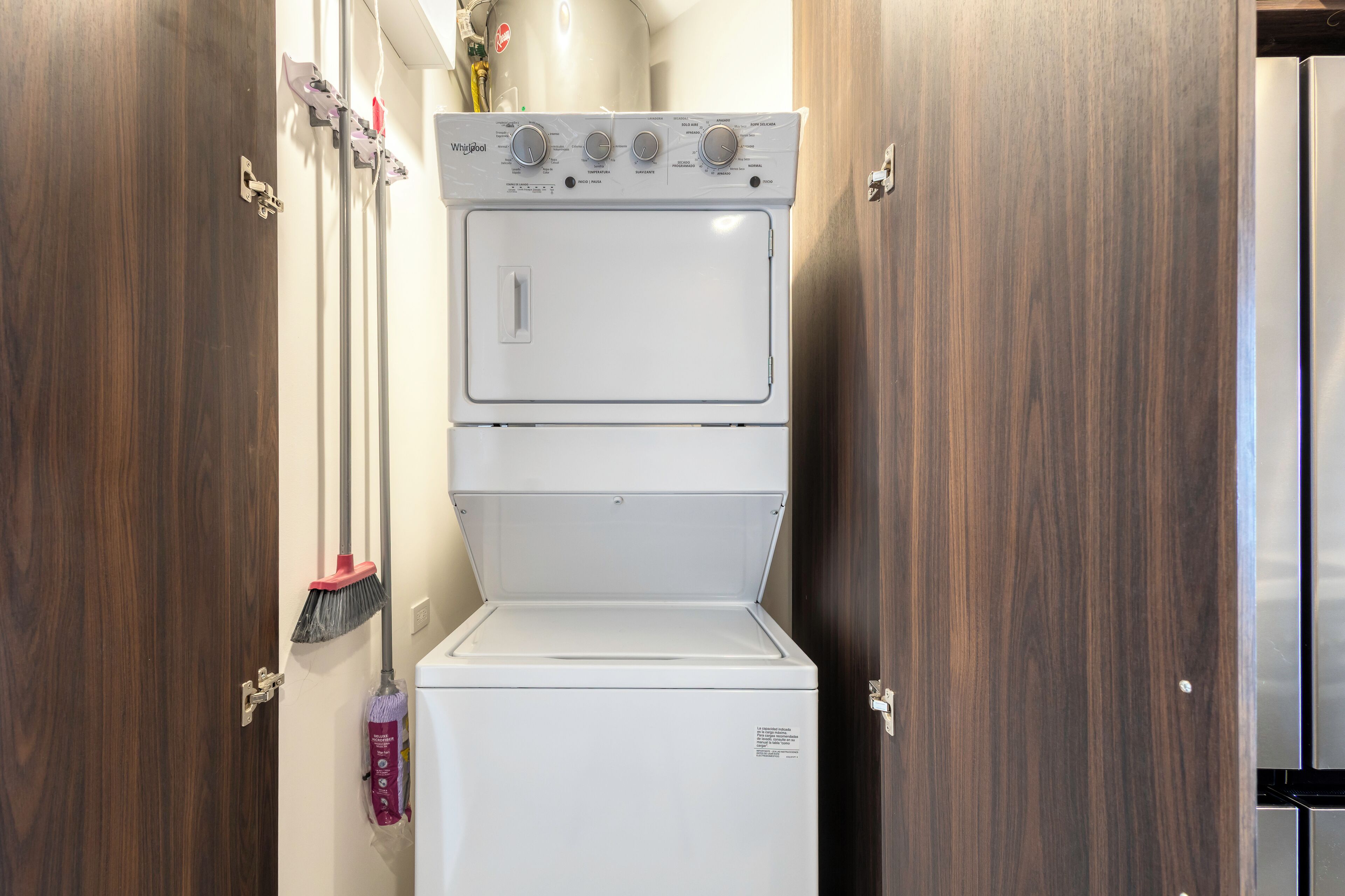 A stacked washer and dryer unit in a narrow hallway with wooden doors.