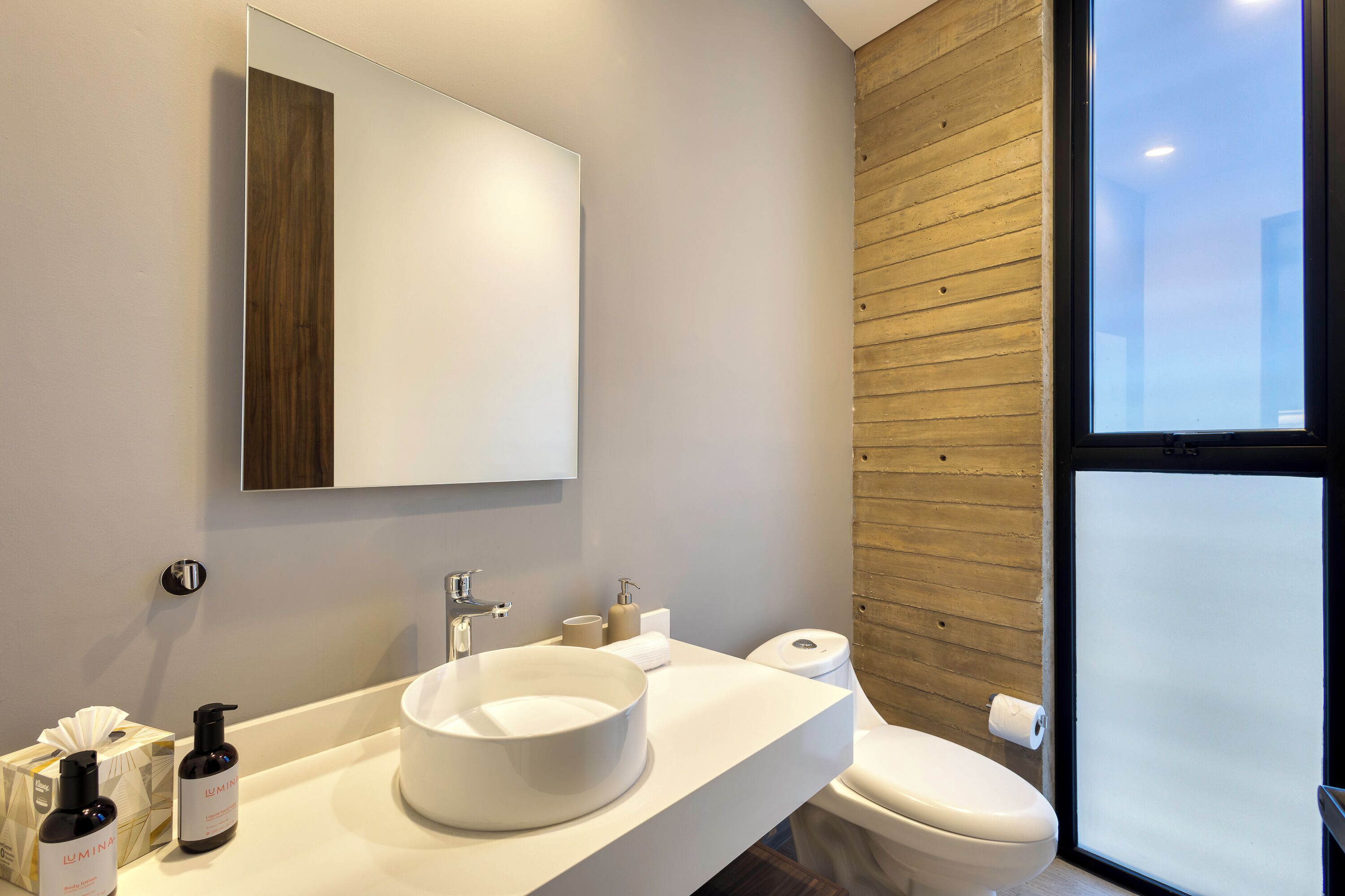 A modern bathroom with a large mirror, a round sink, and a toilet.