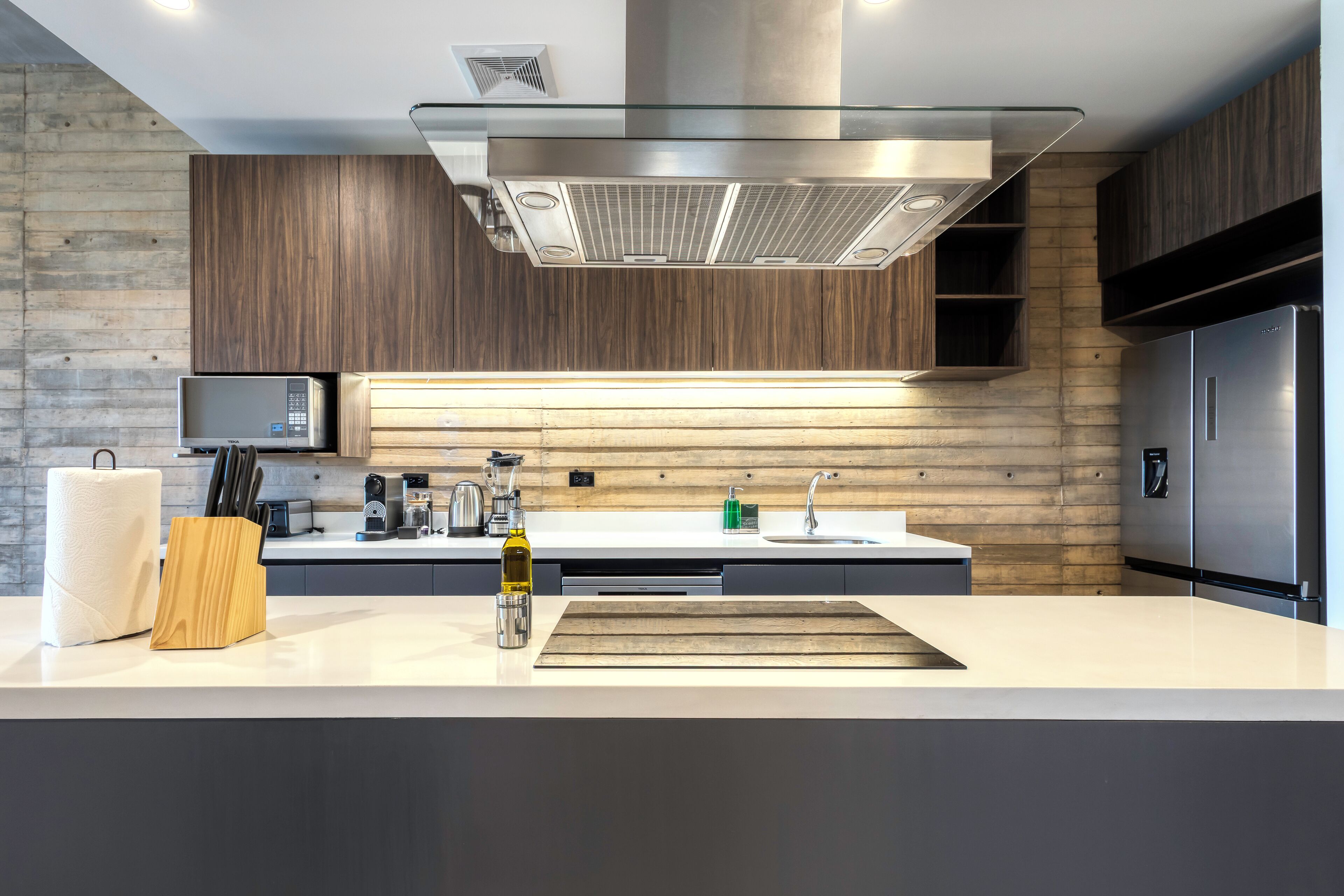 A modern kitchen with a central island, stainless steel appliances, and wooden paneling on the walls.