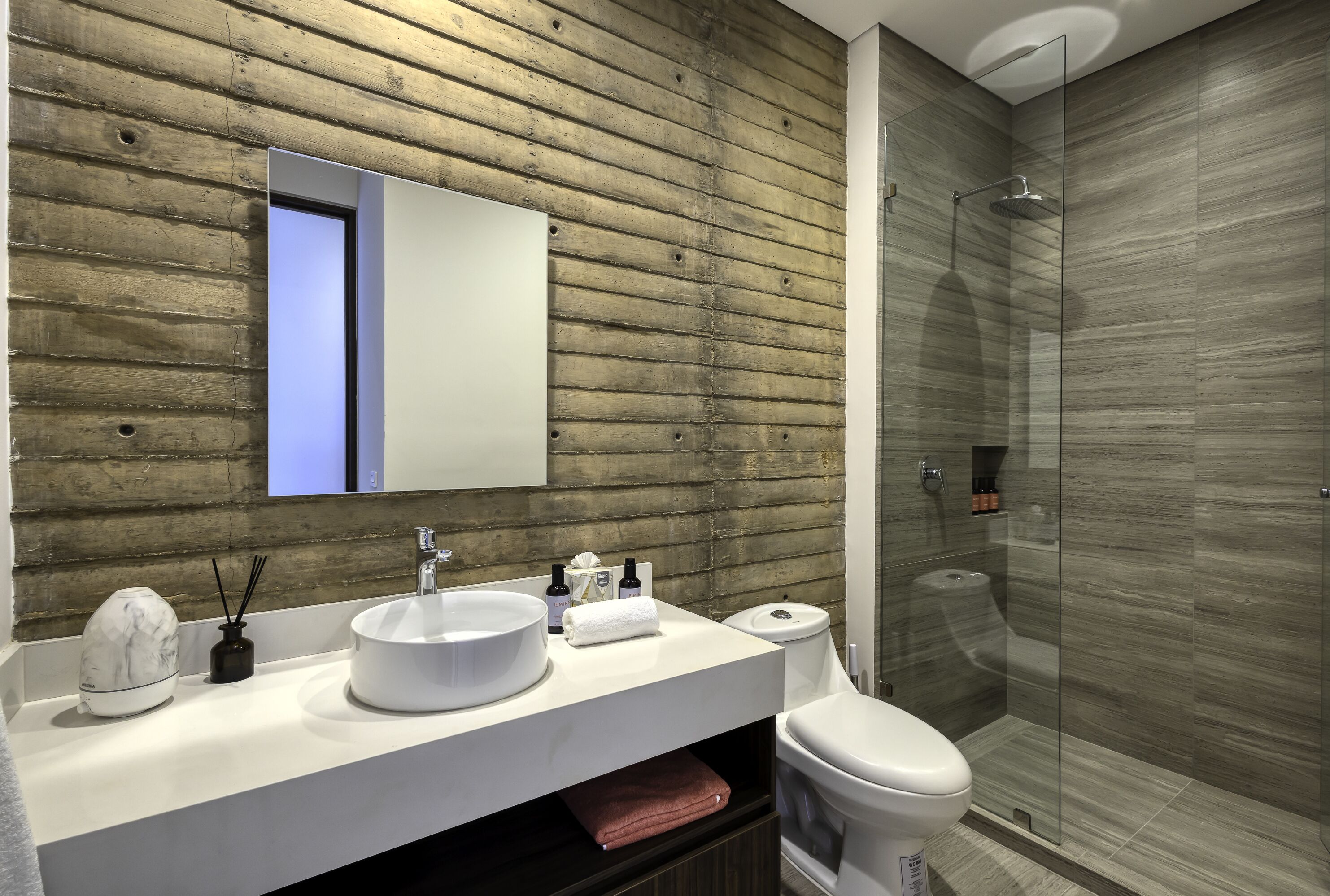 Une salle de bain moderne avec un mur en bois, un grand miroir, un lavabo rond, des toilettes et une douche à parois de verre.