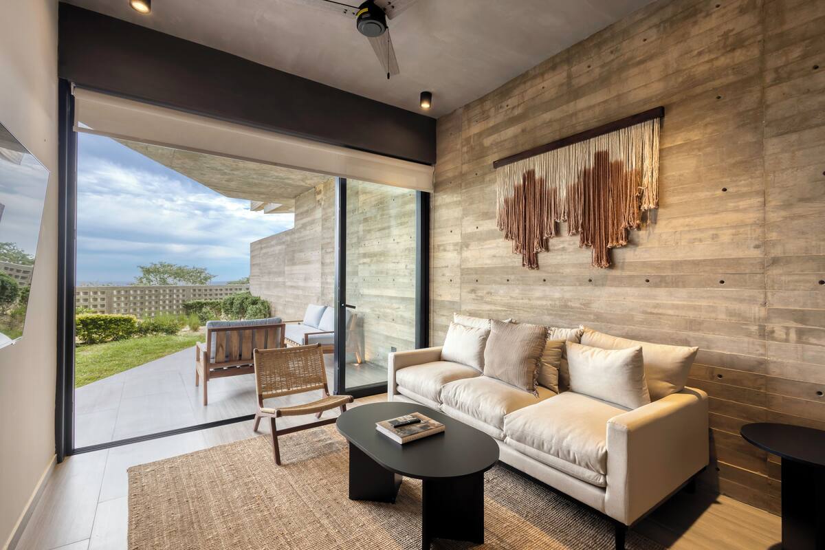 A modern living room with a large window, a sofa, a coffee table, and a hanging macrame piece.