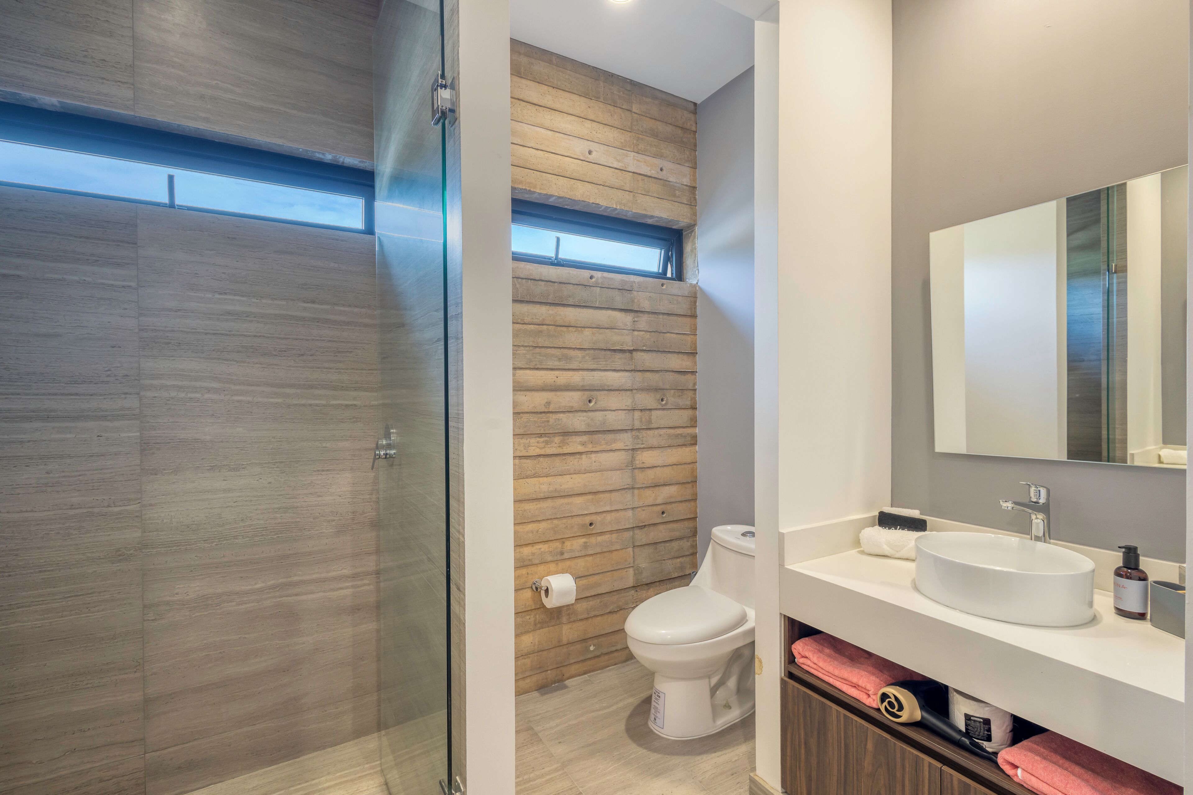 A modern bathroom with a glass shower enclosure, a wooden wall, a toilet, and a vanity with a sink and mirror.