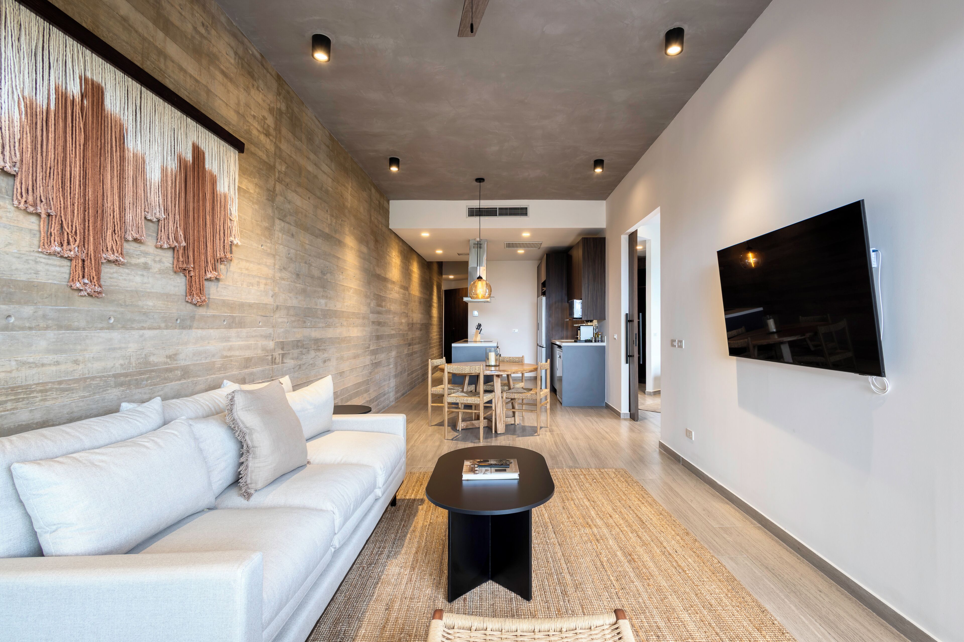 A modern living room with a white sofa, a black coffee table, and a large TV mounted on the wall.