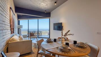 A modern dining area with a wooden table set for four, a sofa, and a view of the ocean through large windows.