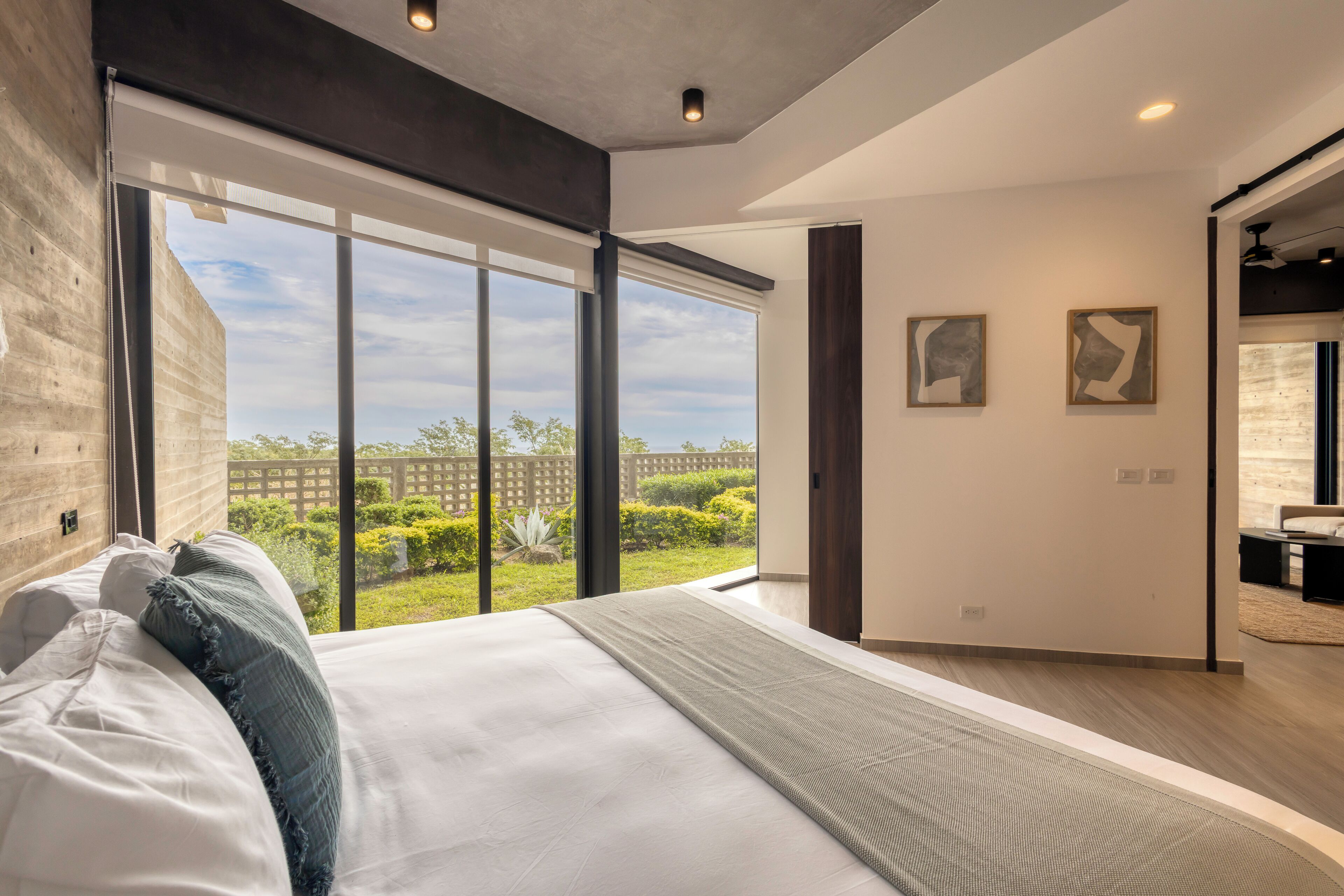 A modern bedroom with a large bed, a view of the outdoors, and two abstract paintings on the wall.