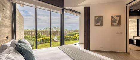 A modern bedroom with a large bed, a view of the outdoors, and two abstract paintings on the wall.