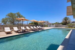 A swimming pool with lounge chairs and umbrellas, surrounded by a stone wall and trees. - OR Cabo Boutique Residences by Lumina (Cabo San Lucas)