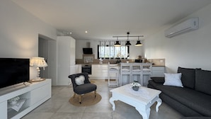 A modern living room with a TV, sofa, and coffee table. There is a kitchen in the background with a dining area. - House in Ruaudin Near Le Mans Circuit (Ruaudin)