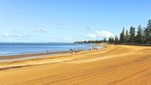 A wide sandy beach with a clear blue sky and calm sea. - "Salt-Air Serenity" (Redcliffe)