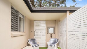A small patio with two wicker chairs, a white door, and a window with a metal screen. - "Salt-Air Serenity" (Redcliffe)