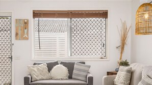 A modern living room with a grey sofa set, a round coffee table, and a large window with blinds. - "Salt-Air Serenity" (Redcliffe)
