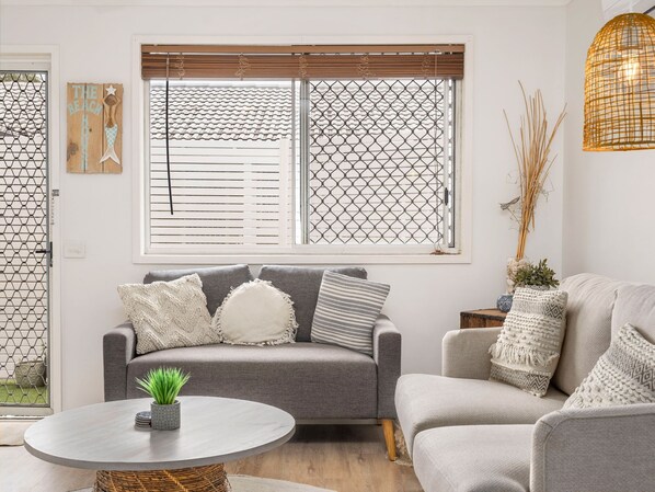 A modern living room with a grey sofa set, a round coffee table, and a large window with blinds.