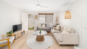 A modern living room with a grey sofa, a round coffee table, a TV on a wooden stand, and a ceiling fan. - "Salt-Air Serenity" (Redcliffe)