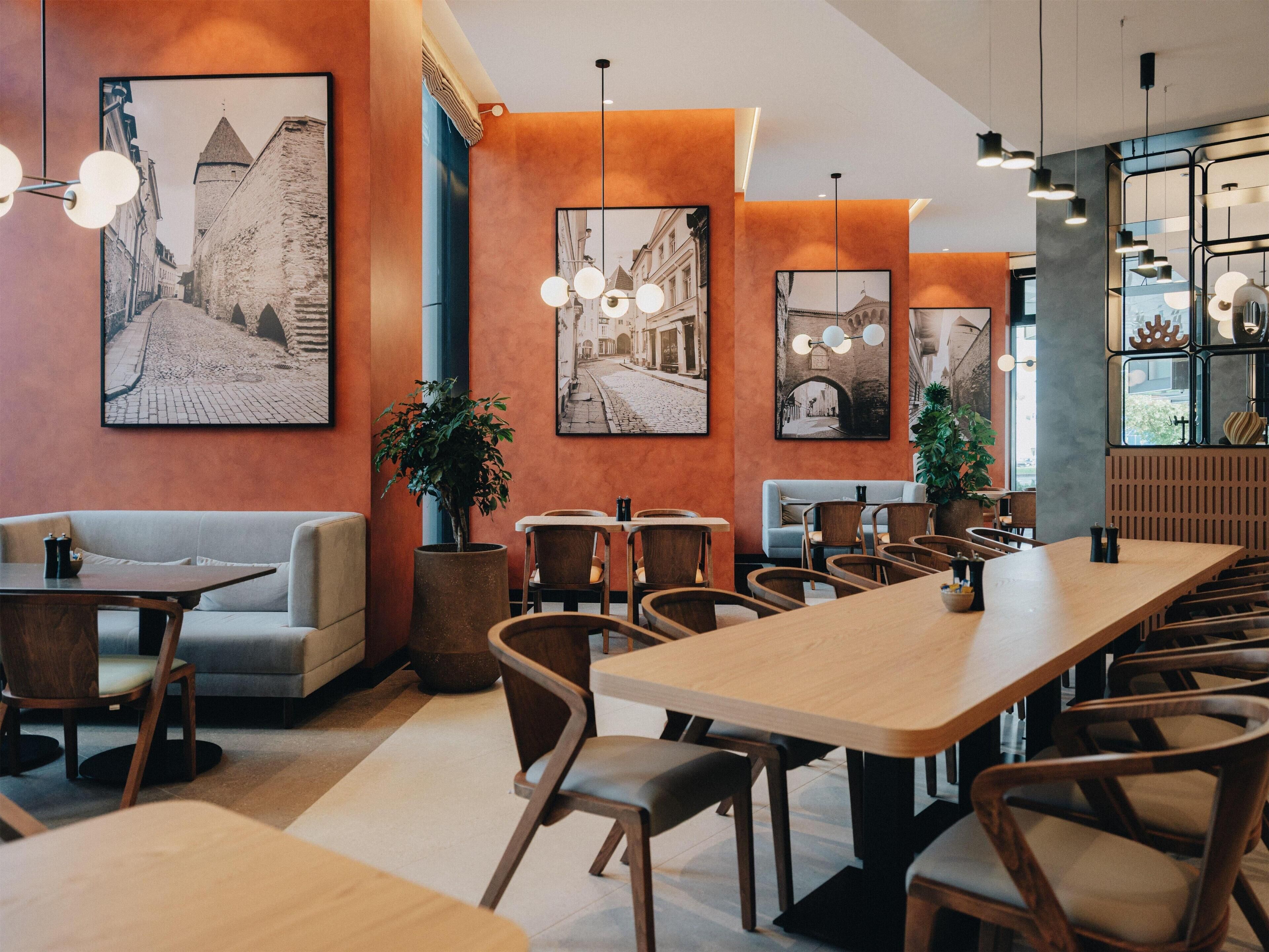 Ein modernes Restaurantambiente mit Holztischen und -stühlen, großen gerahmten Fotografien an den Wänden und Pendelleuchten.
