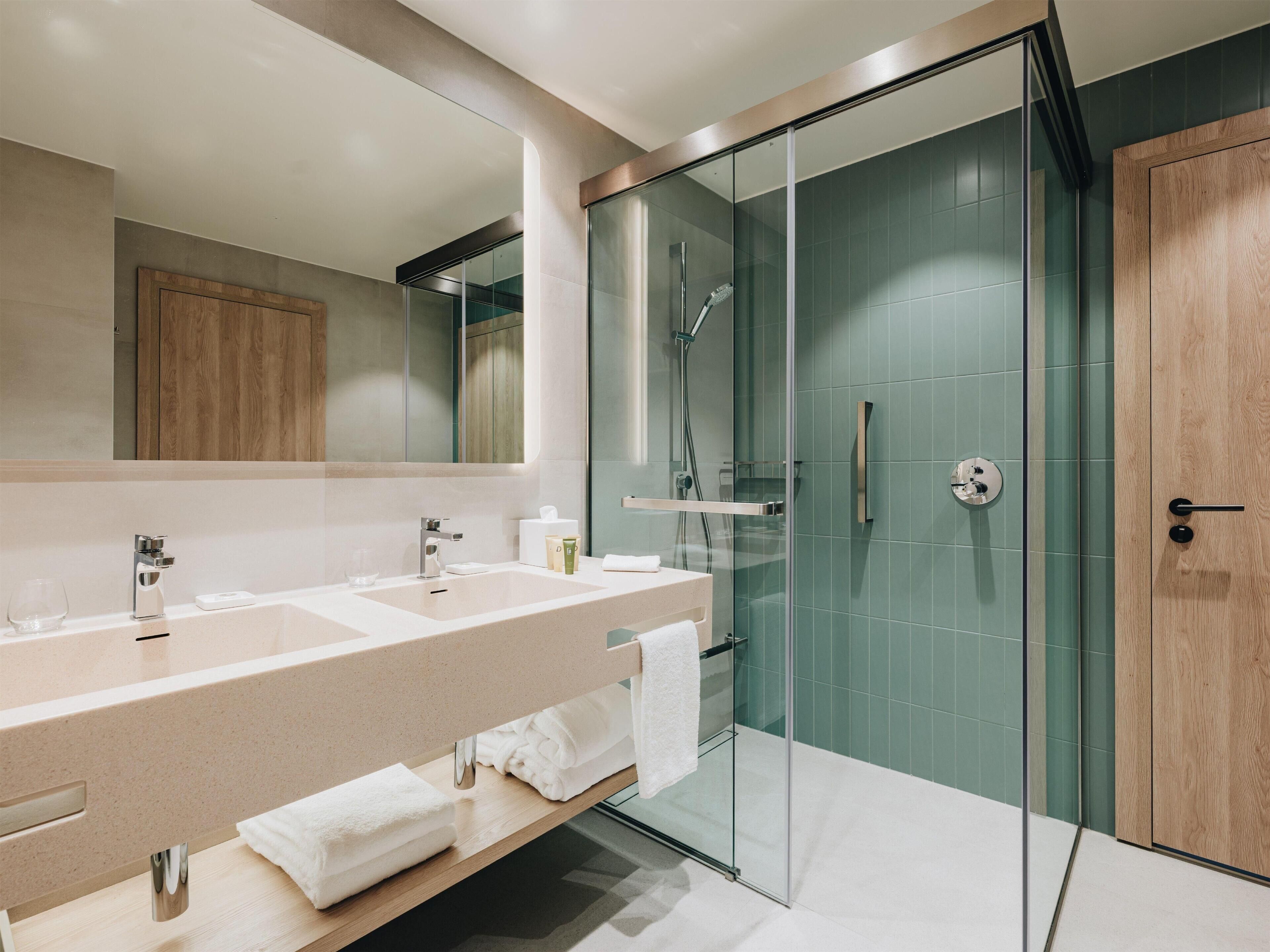 Un baño moderno con ducha de vidrio, un espejo grande y tocador con lavamanos y toallero.