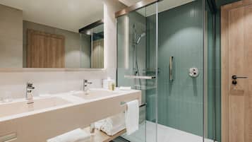 Un baño moderno con ducha de vidrio, un espejo grande y tocador con lavamanos y toallero.