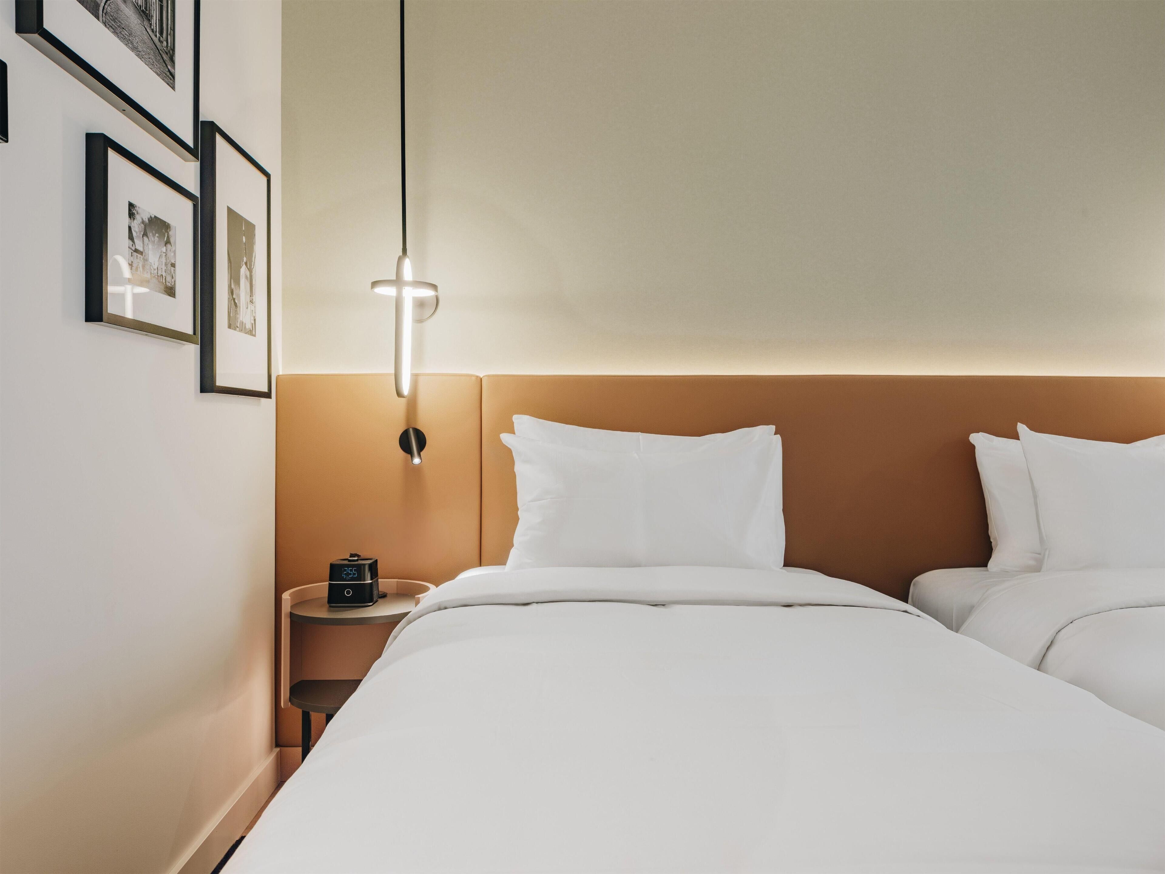 A hotel room with a bed, bedside table, and a wall-mounted light fixture.
