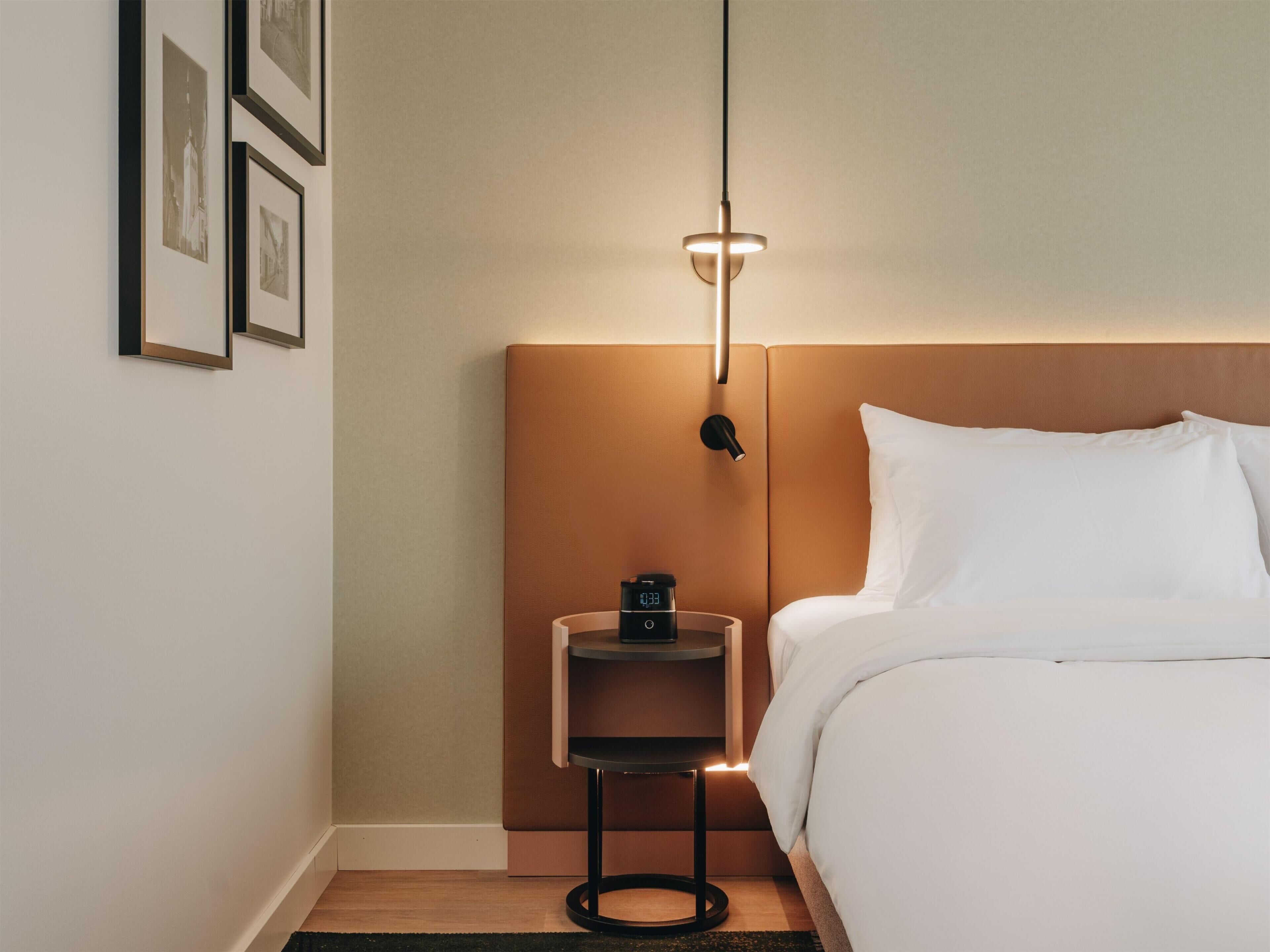 Una habitación de hotel con una cama, una mesita de noche con una lámpara y cuadros en la pared.