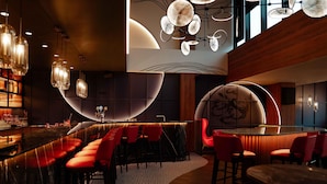 A modern bar area with a curved bar, red bar stools, and pendant lighting.