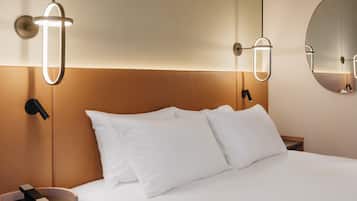 A hotel room with a bed, bedside tables, a round mirror, and wall-mounted lighting fixtures.