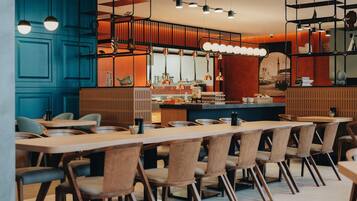 Interior moderno de restaurante con mesas y sillas de madera, iluminación colgante y una zona de bar.