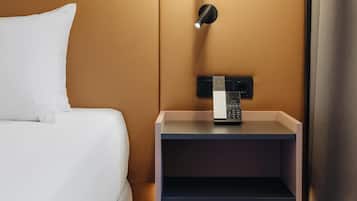 A hotel room with a bed, a bedside table with a phone, and a wall-mounted light fixture.