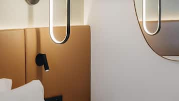 A modern hotel room with a bed, bedside table, and a wall-mounted mirror.