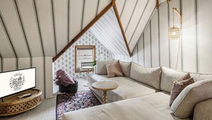 Une chambre à coucher confortable, aménagée en mezzanine, avec un plafond en pente, un canapé, une petite table ronde et un téléviseur.