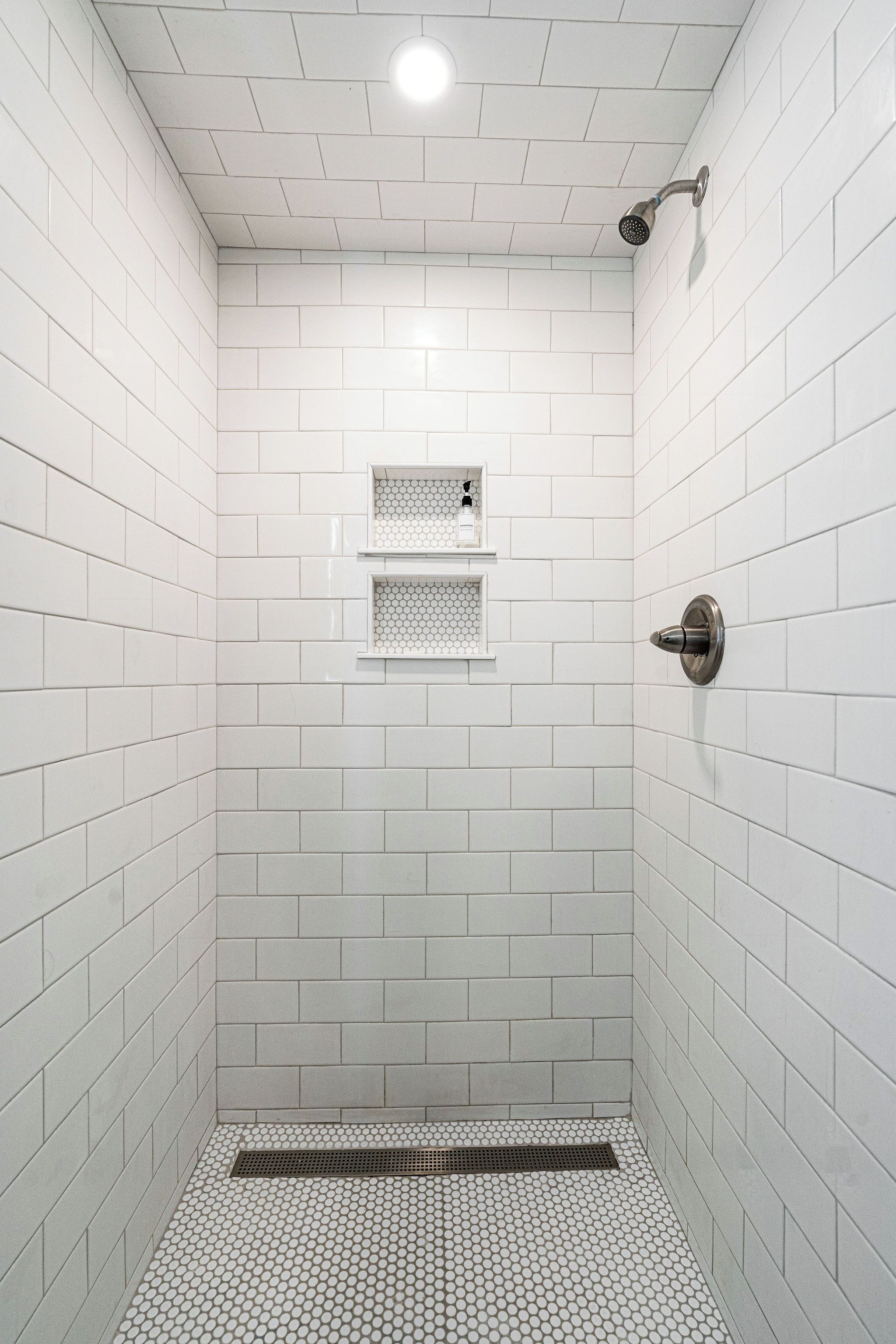 Een douche met witte tegels, een metalen douchekop en een klein plankje.