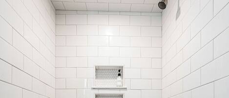 Een douche met witte tegels, een metalen douchekop en een klein plankje.