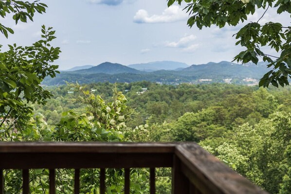 Blick von einer Holzterrasse über eine üppige Landschaft mit fernen Bergen und dichtem Grün.