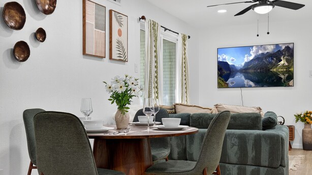 Un coin repas avec une table ronde, des chaises et un canapé. Un tableau est accroché au mur et un ventilateur de plafond est installé au-dessus.