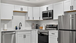 Une cuisine moderne avec des meubles blancs, des appareils en acier inoxydable, un four à micro-ondes, un four et un lave-vaisselle.