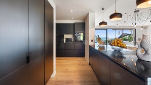 A modern kitchen with dark cabinetry, a wooden floor, and a view of the outdoors.