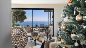 A modern living room with a large window overlooking the sea, furnished with a sofa, chairs, and a coffee table.