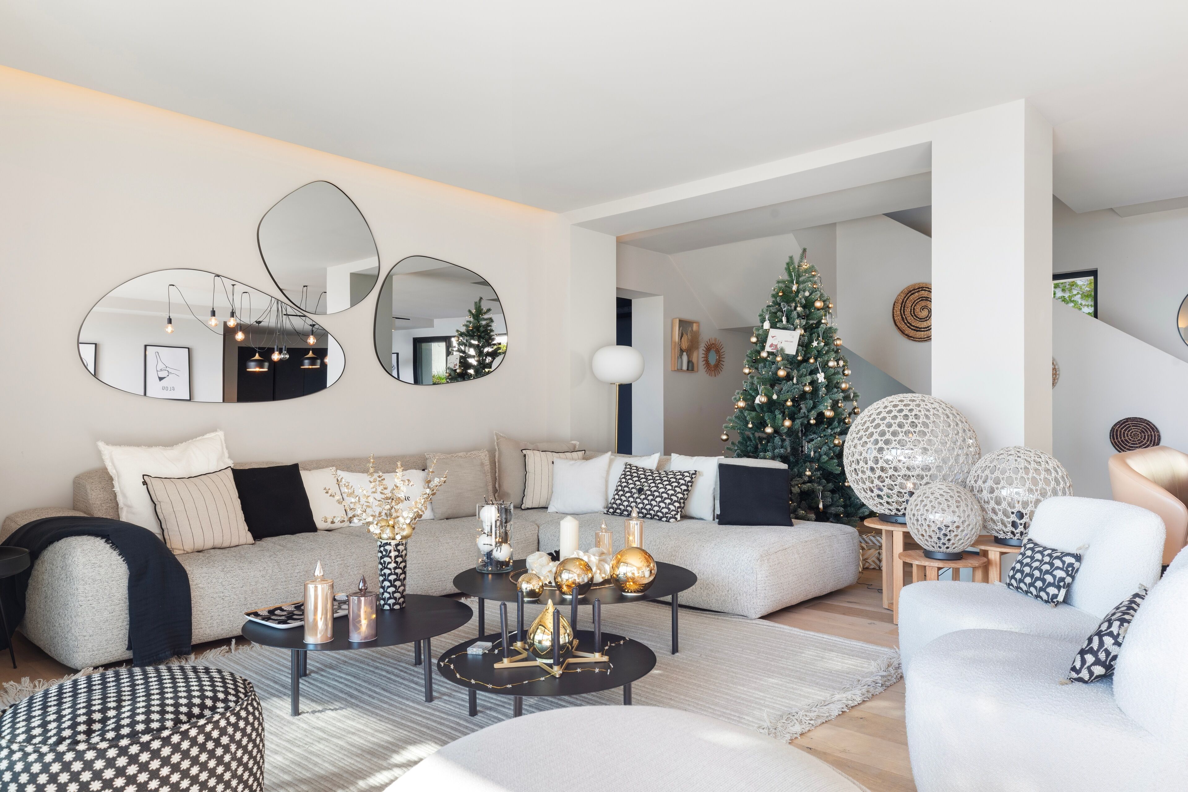 Ein modernes Wohnzimmer mit einer Couch, einem Couchtisch und dekorativen Spiegeln. Im Hintergrund ist ein Weihnachtsbaum zu sehen.