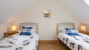 Une chambre avec deux lits, une petite fenêtre, un plancher en bois et des lampes de chevet.
