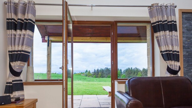 A room with a sliding glass door leading to a patio, a brown leather chair, and a small wooden table with books. - 2 Eden Cottage - sleeps 8 guests  in 3 bedrooms (Linlithgow)