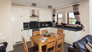 A compact kitchen with white cabinets, a wooden dining table, and a leather sofa. - 2 Eden Cottage - sleeps 8 guests  in 3 bedrooms (Linlithgow)