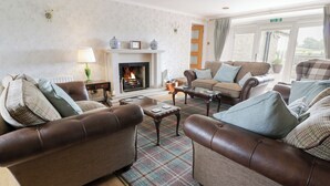 A cozy living room with leather sofas, a fireplace, and a plaid rug. - Marshill Farm House (Lanark)