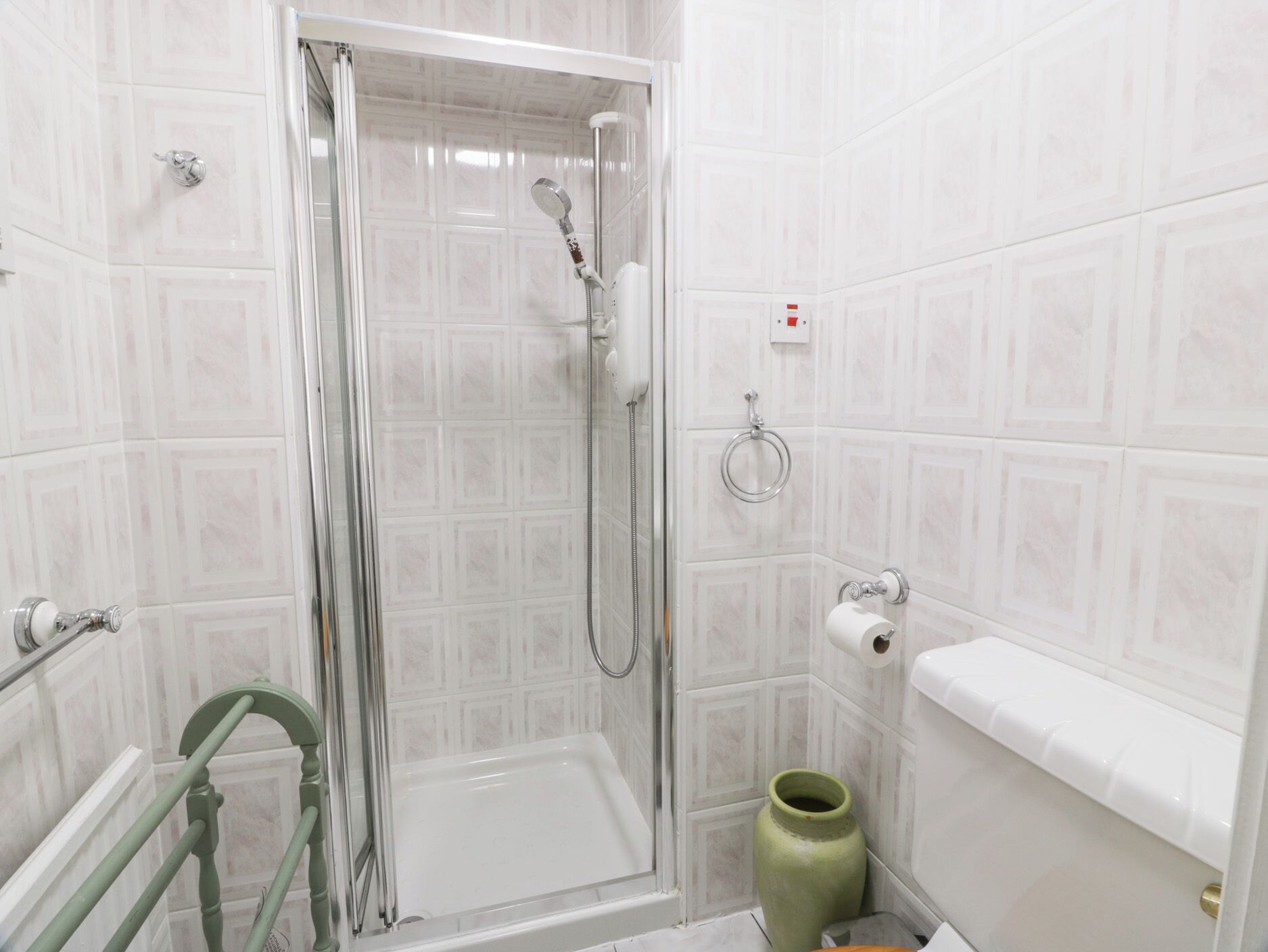 A bathroom with a glass-enclosed shower, a toilet, and a green vase.